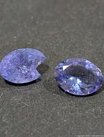 Two faceted tanzanite gemstones on dark surface