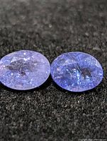 Two loose faceted oval tanzanite gemstones on dark background