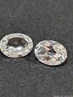 Close-up of two oval faceted white topaz stones on dark background