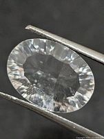 Oval white topaz held in tweezers showing facets