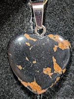 Front view of heart-shaped mahogany obsidian pendant showing black surface with reddish-brown patches and attached bail