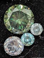 Four loose moissanite gemstones on dark background, largest showing green tint