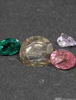 Four loose faceted gemstones in various colours and cuts on dark background