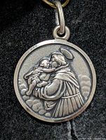 Obverse of round silver pendant showing saint and infant with halo, clouds background