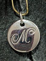 Front view showing script "M" engraving on round pendant