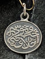 Front view of oval silver pendant with raised calligraphy