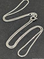 Full view of silver box chain necklace coiled on black background