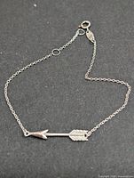 Entire bracelet laid flat showing arrow charm, chain, clasp and extender rings