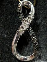 Front view of silver infinity pendant showing three diamonds and dark stone accents