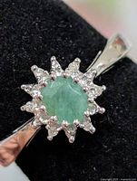 Front view of ring showing emerald center and clear halo