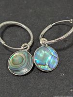 Front view of the pair of silver hoop earrings with round abalone mother of pearl drops