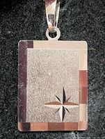 Front view of rectangular silver pendant showing brushed center, star cutout, polished border, bail
