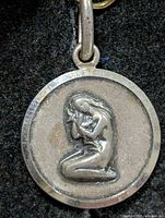 Front view of round silver pendant showing kneeling woman relief and bail