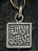 front view of square silver pendant showing Arabic inscription and bail