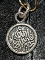Front view of round silver pendant showing full Arabic inscription and loop