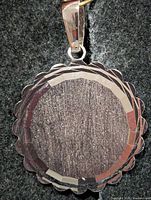 front view of circular silver pendant showing scalloped edge and faceted border