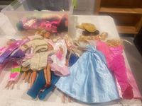 Eight Barbie dolls laid out with various outfits, accessories and clear tote containing more clothes