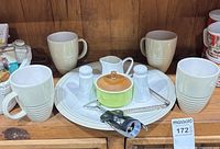 Full view of mugs, plates, creamer, sugar bowl, shakers, corkscrew and cheese plane arranged on shelf