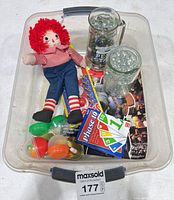 Overall lot in bin showing doll, mugs of marbles, Phase 10, capsule toys