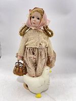 Full view of doll with clothing, basket and goose stand