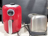 Front view of red Dash mini air fryer beside stainless steel two-slice toaster