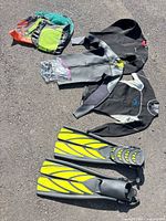 Overview of wetsuits, fins, hood, bags, snorkels on pavement