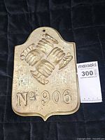 Front view of brass fire mark showing clasped hands design and No. 906 inscription