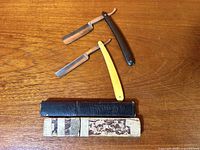 Two straight razors with both storage boxes displayed on wood surface