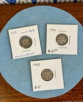 Front view of three coins in flips displaying obverse details and handwritten year/price