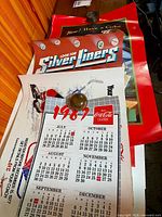 Stack showing multiple Coca-Cola posters including Silver Liners and 1987 calendar sheet