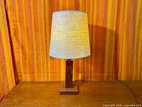 Full view of teak lamp with shade on a teak surface