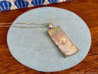 Front view of pendant on chain showing iridescent mother-of-pearl surface and pearl accent