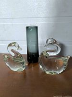 two clear glass swans and grey smoked bud vase displayed together