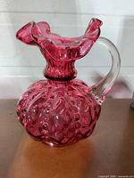 Front view of cranberry glass vase showing handle and textured body