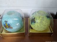 Pair of sealed boxed spherical candles, aqua and yellow-green, insect motifs visible