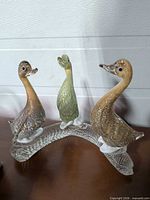 Full view of three glass ducks on clear curved base