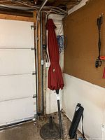 Umbrella folded on base with carry bag leaning on wall