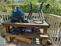 Overall view of Big Green Egg grill on wooden table with metal stand frame and charcoal bags