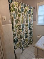 Full view of shower curtain hanging with pattern visible and waste bin below
