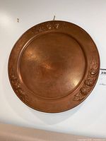 Full view of round hammered copper charger with floral rim