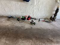 Wide shot showing EGO trimmer components, battery, charger, line spool and Troy-Bilt gas trimmer