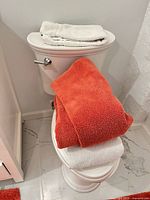 Towels stacked on toilet lid in orange and off-white colors