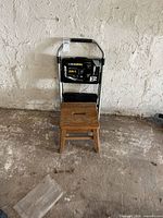 Front view of ladder folded behind wooden stool