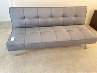Front view of gray tufted futon sofa with metal legs