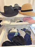 Shelf with black felt hat, tan straw hat, multiple caps and beanies visible