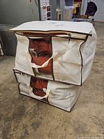 Two cream zippered storage bags stacked, each showing orange rust cushions through vinyl window