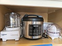 Front view of Cuisinart food processor, Aroma rice cooker, Elite juicer and partial Crock-Pot on shelf