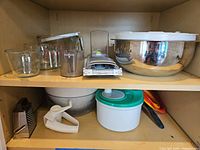 cabinet shelf showing glass measuring cups, mandoline chopper, stainless bowls with lids
