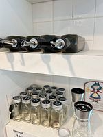 Overview of oil bottles on upper shelf, spice jars, grinders and plaque on lower shelf