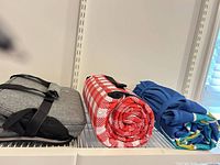 Three folded/rolled mats on shelf: gray case, red gingham roll, blue roll